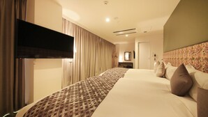 A hotel room with a large bed, a flat-screen TV mounted on the wall, and a floral-patterned headboard.