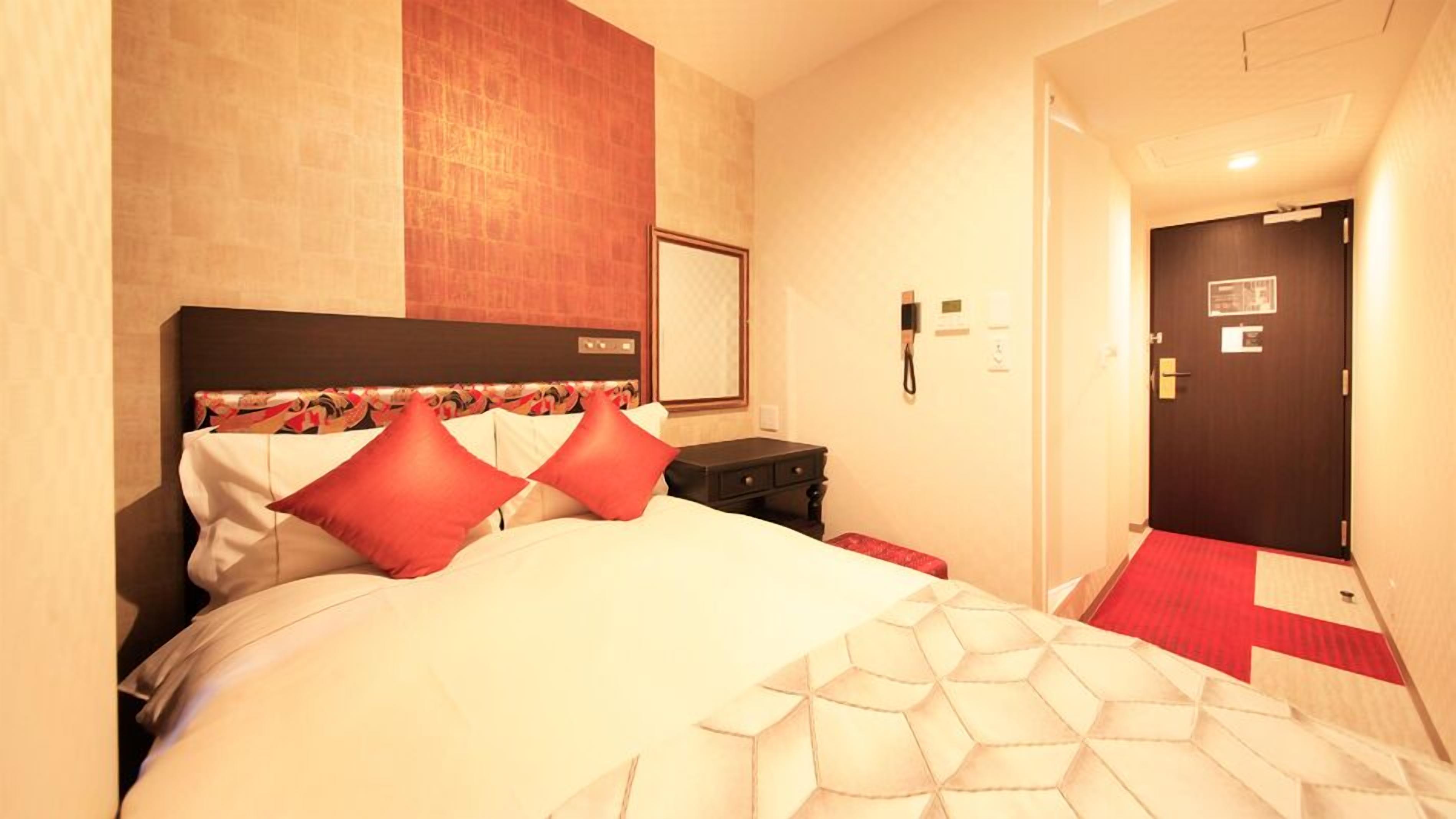A hotel room with a bed, a nightstand, a phone, and a door.