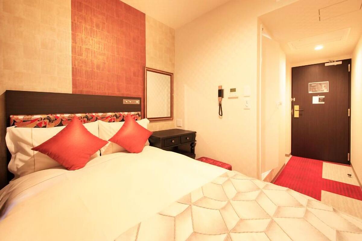 A hotel room with a bed, a nightstand, a phone, and a door.