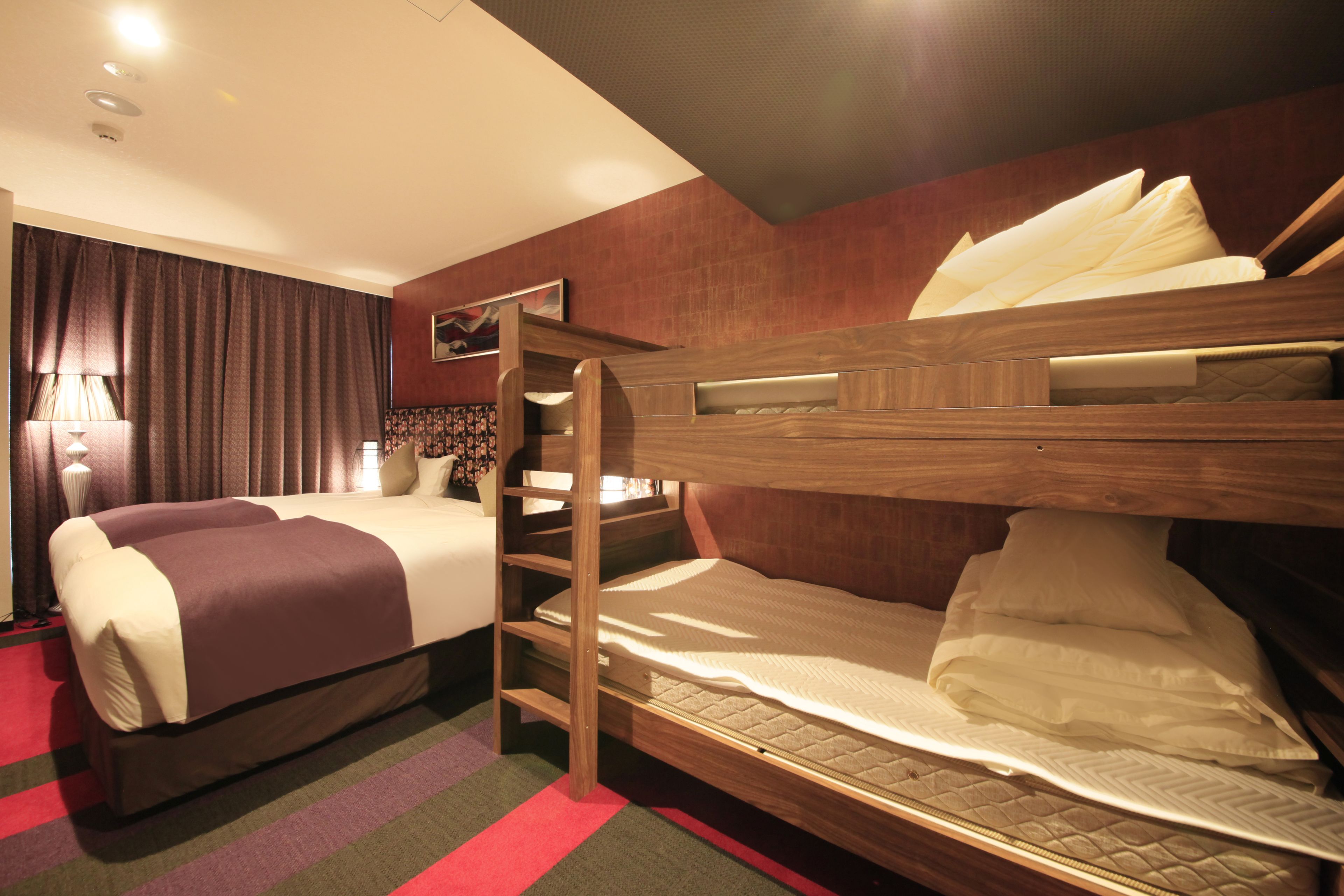 A hotel room with a bunk bed, a desk, and a large window with curtains.