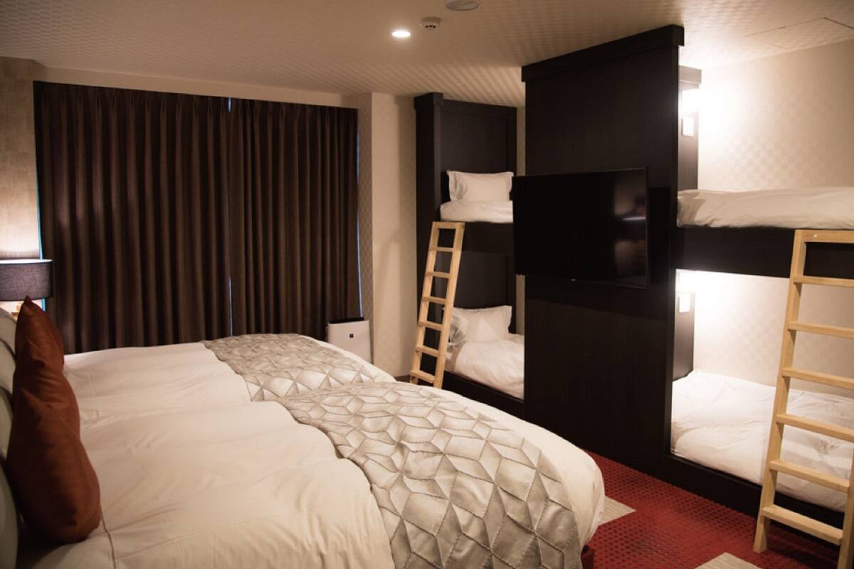 A hotel room with a large bed, two bunk beds, a TV, and a red carpet.