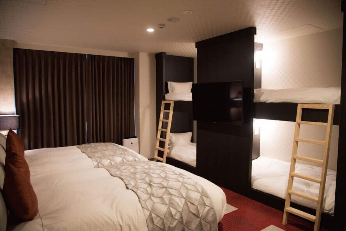 A hotel room with a large bed, two bunk beds, a TV, and a ladder.