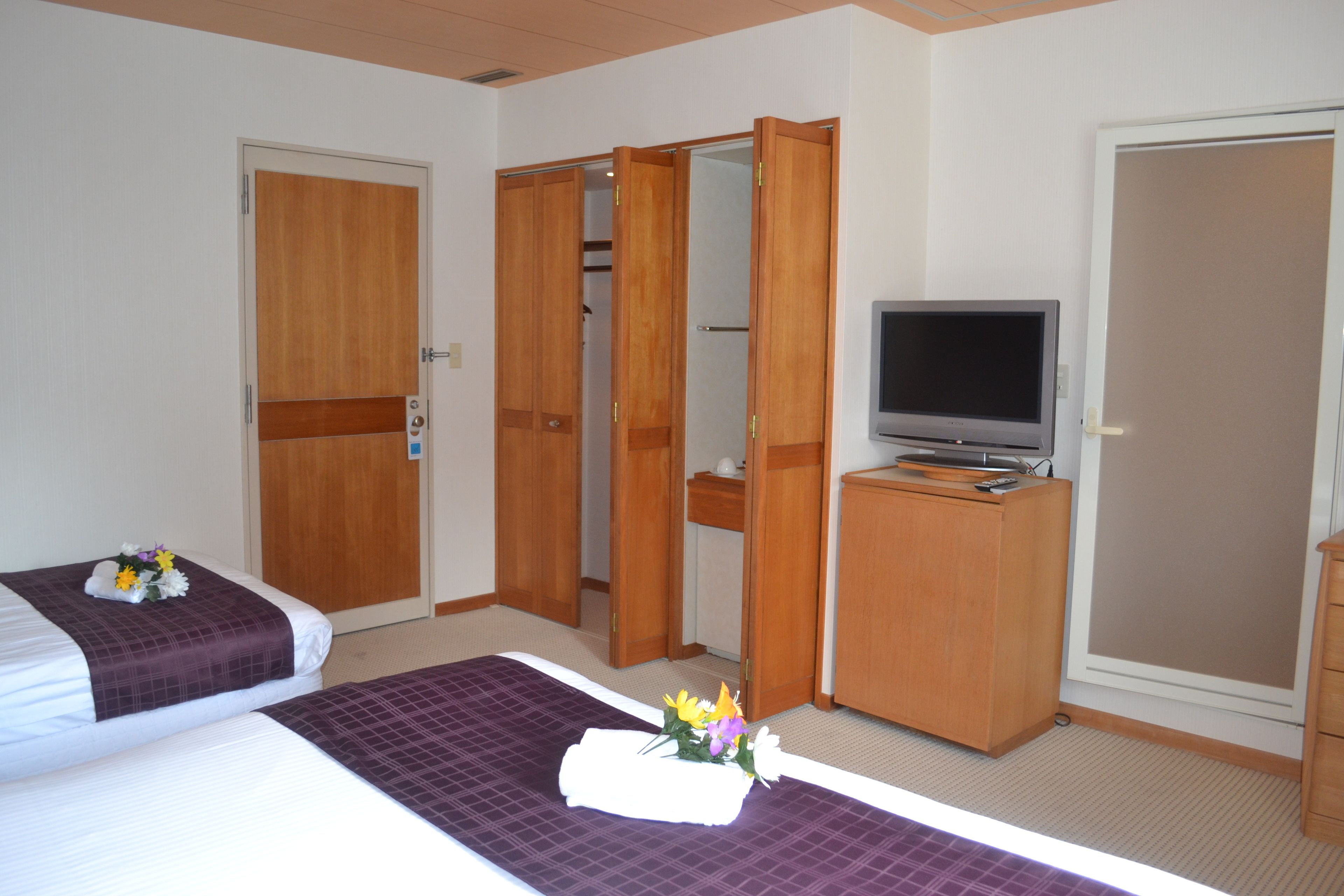 A hotel room with two beds, a television, a wardrobe, and a bathroom.