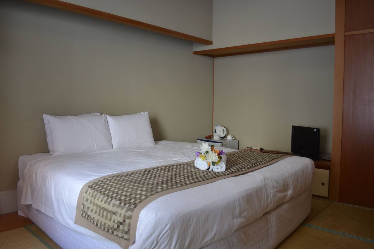 A neatly made bed with white linens, a patterned throw blanket, and a small bouquet of flowers on the bed.