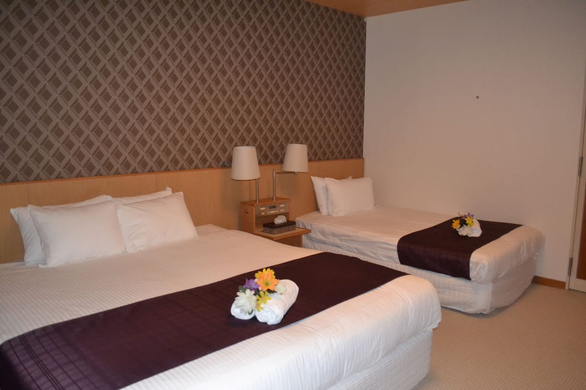 A hotel room with two beds, each with white linens and a dark brown bedspread. There are two bedside lamps on wooden nightstands.
