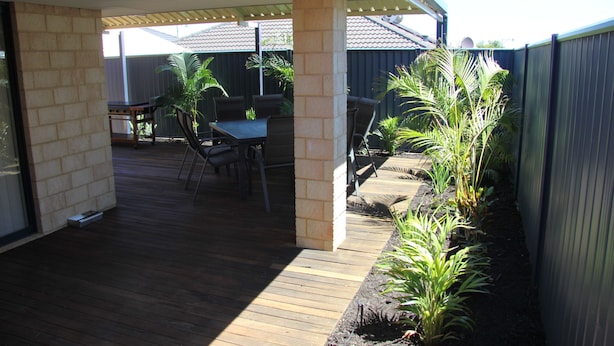 Un patio couvert avec une terrasse en bois, du mobilier d’extérieur et un pilier en briques.