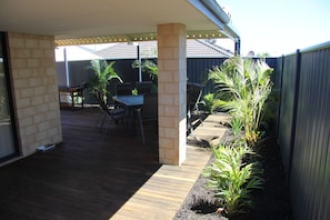 Un patio cubierto con terraza de madera, mobiliario exterior y un pilar de ladrillo.