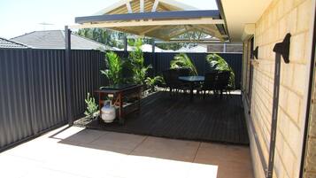 A covered patio area with a table and chairs, surrounded by a metal fence and potted plants.
