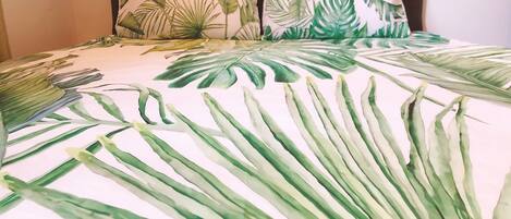 Un lit avec une couvre-lit ornée d’un motif de feuilles tropicales et des coussins assortis.