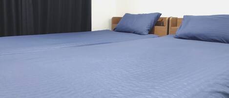 Une chambre avec deux lits, chacun recouvert d’une courtepointe bleue et agrémenté d’oreillers assortis.