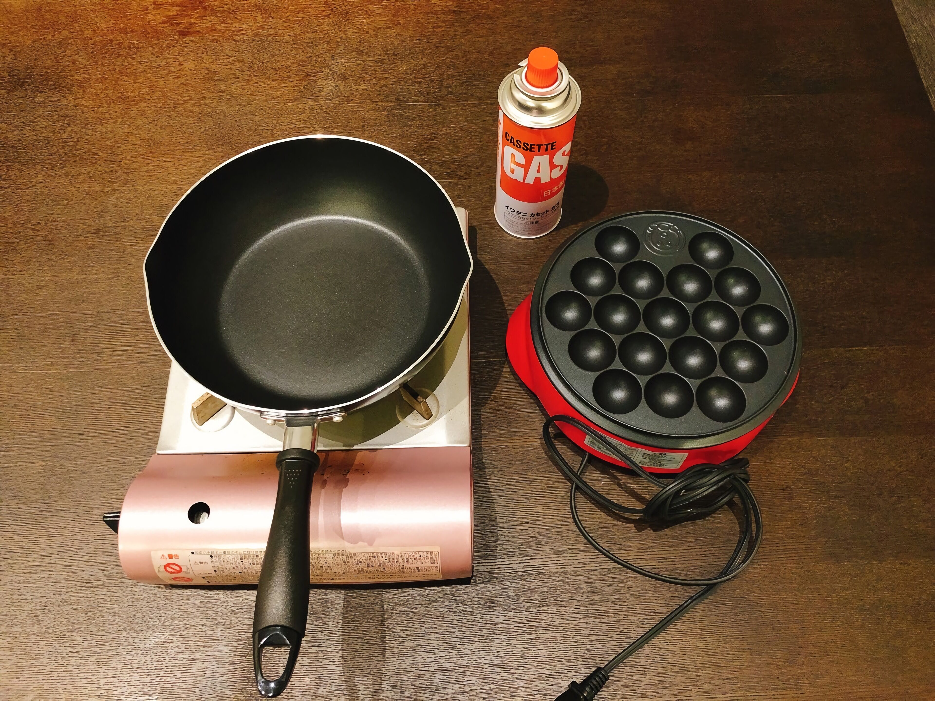 A portable gas stove with a frying pan and a waffle maker on a wooden table.