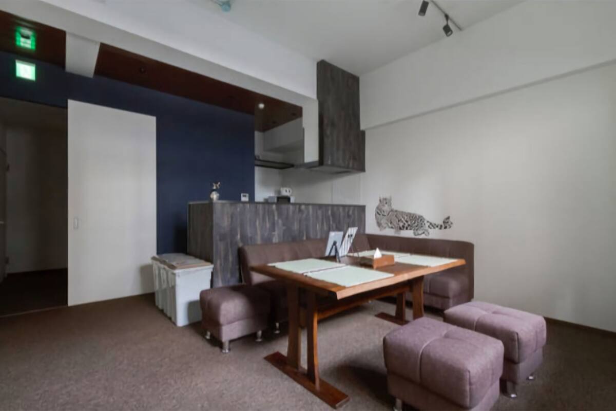 A modern room with a wooden table, two cushioned seating areas, a white cabinet, and a wall-mounted shelf.