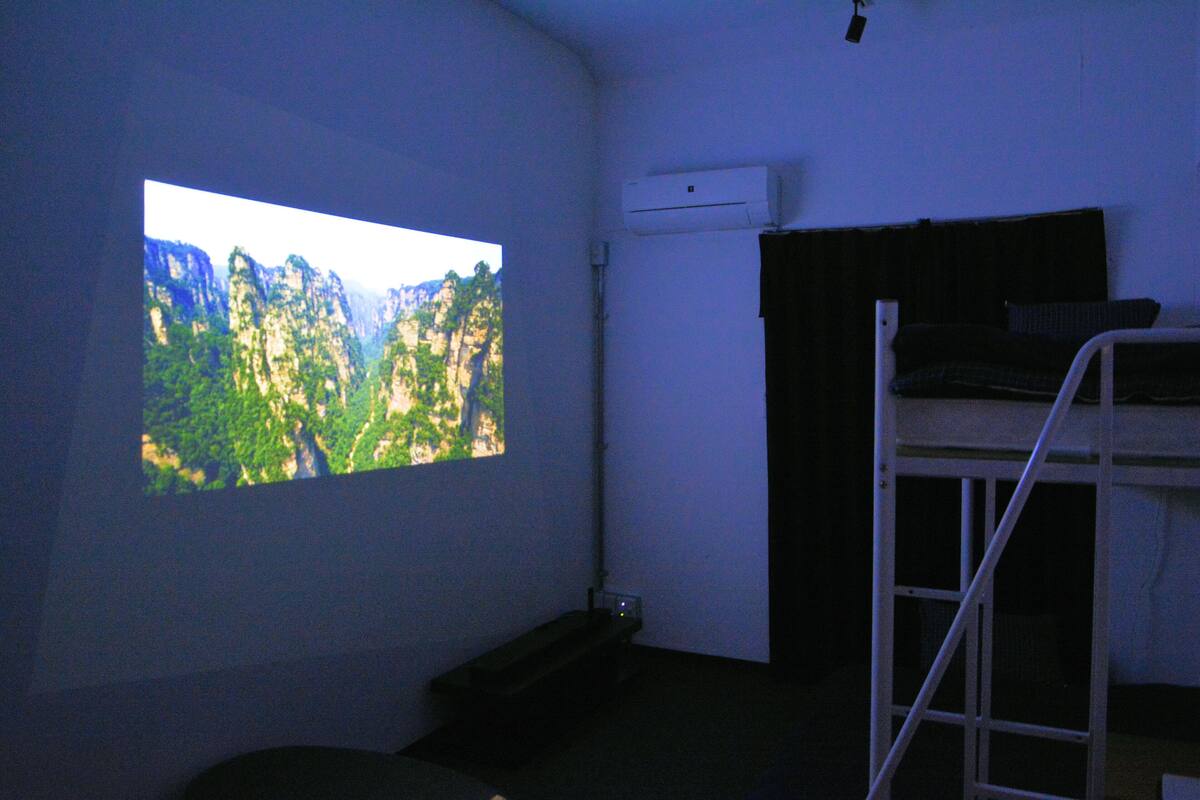 A room with a bunk bed, a projector screen displaying a natural landscape, and an air conditioning unit on the wall.