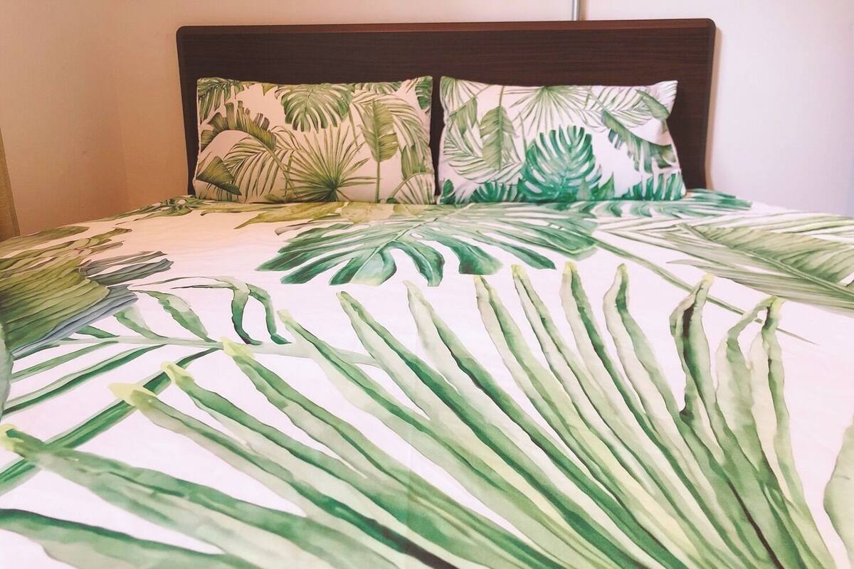 A bed with a tropical leaf pattern bedspread and matching pillows.