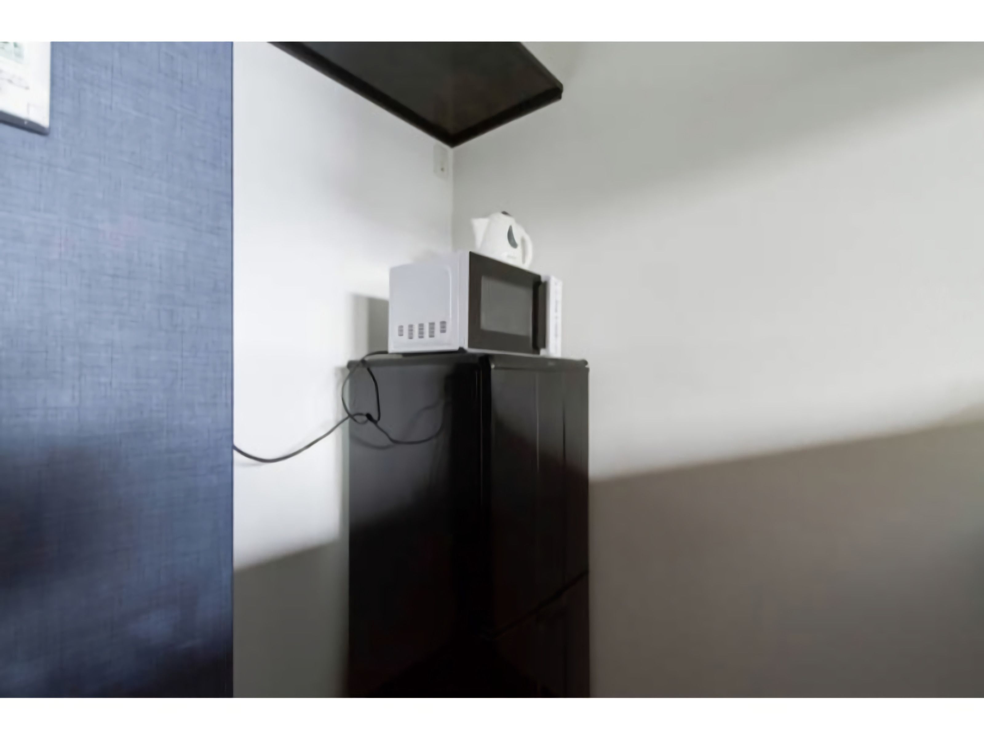 Un four à micro-ondes blanc est posé sur un meuble noir dans une pièce dont le mur est blanc et le sol foncé.