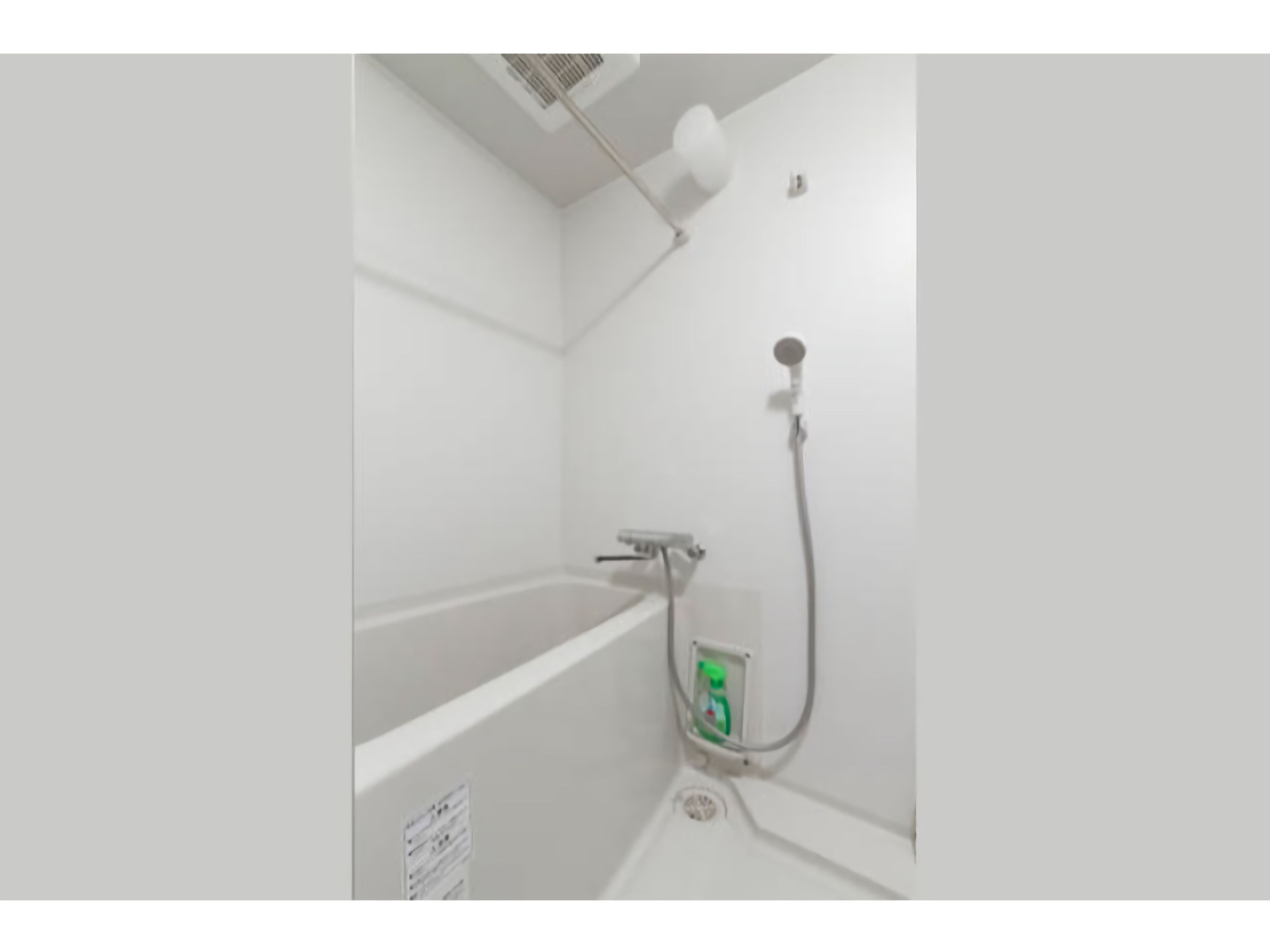 A bathroom with a bathtub, a shower, and a green bottle of shampoo.
