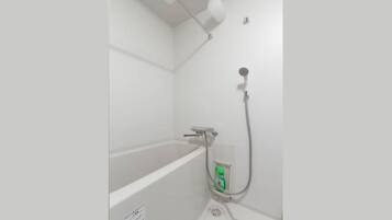 A bathroom with a bathtub, a shower, and a green bottle of shampoo.