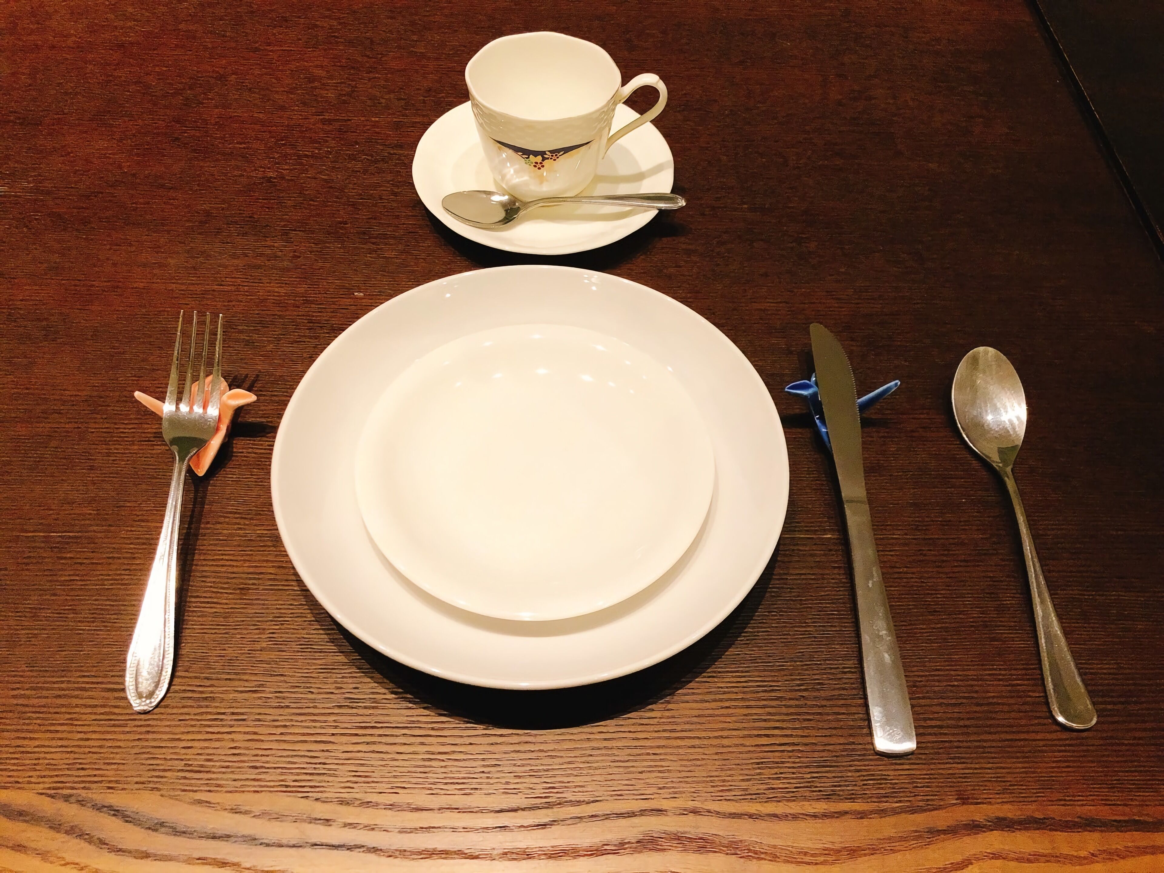 A dining table set with a white plate, a cup, and cutlery.