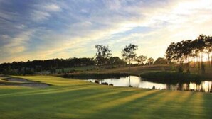 Un campo de golf con un estanque, árboles y cielo despejado.