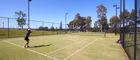 A tennis court with a net, surrounded by a fence, and trees in the background.