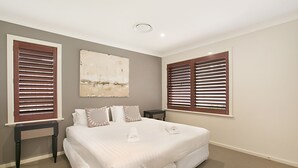 Un dormitorio con una cama grande, dos mesitas de noche y dos ventanas con persianas de madera.