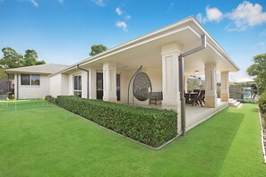 Una casa moderna con un porche cubierto, una piscina y un césped bien cuidado.