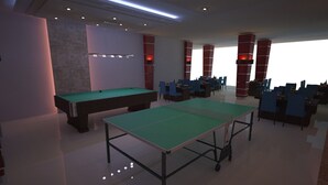 Een biljartkamer met twee pooltafels, blauwe stoelen en rode zuilen.