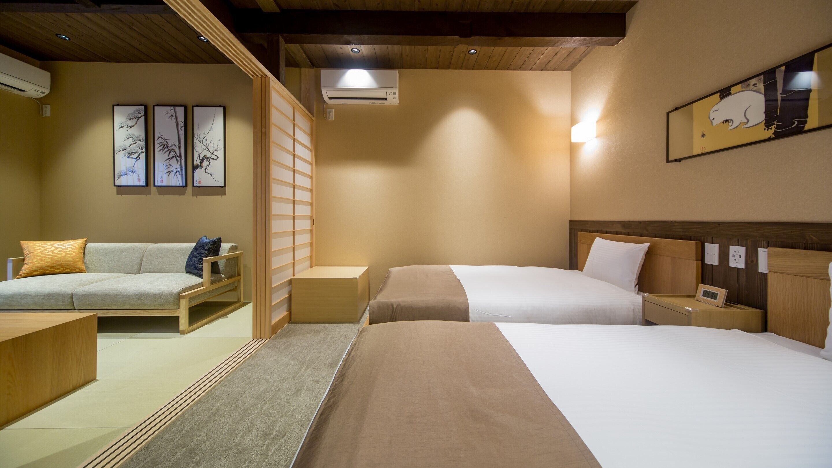 A hotel room with two beds, a sofa, a wooden partition, and artwork on the walls.