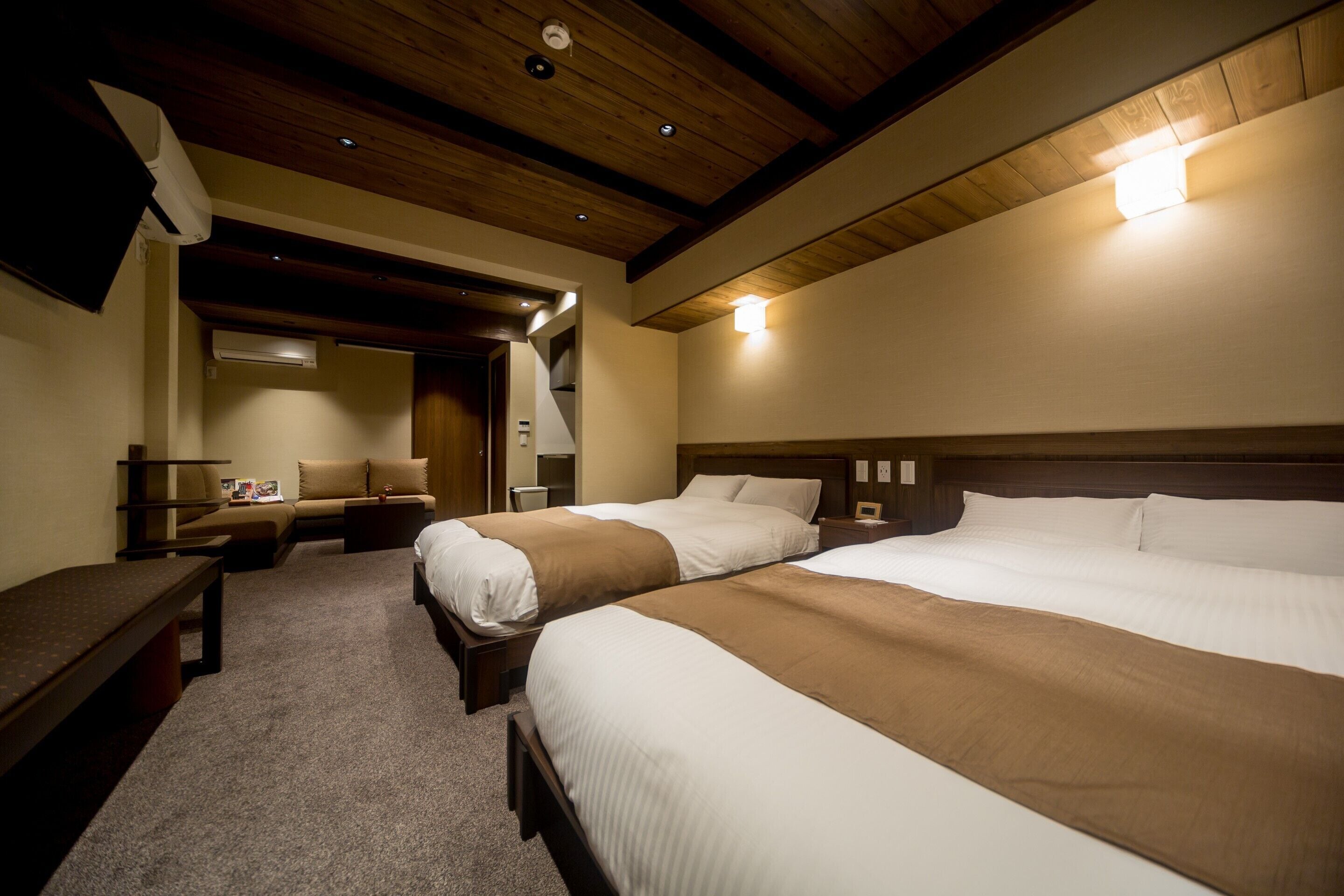 A hotel room with two beds, a bench, a desk, and a lamp.