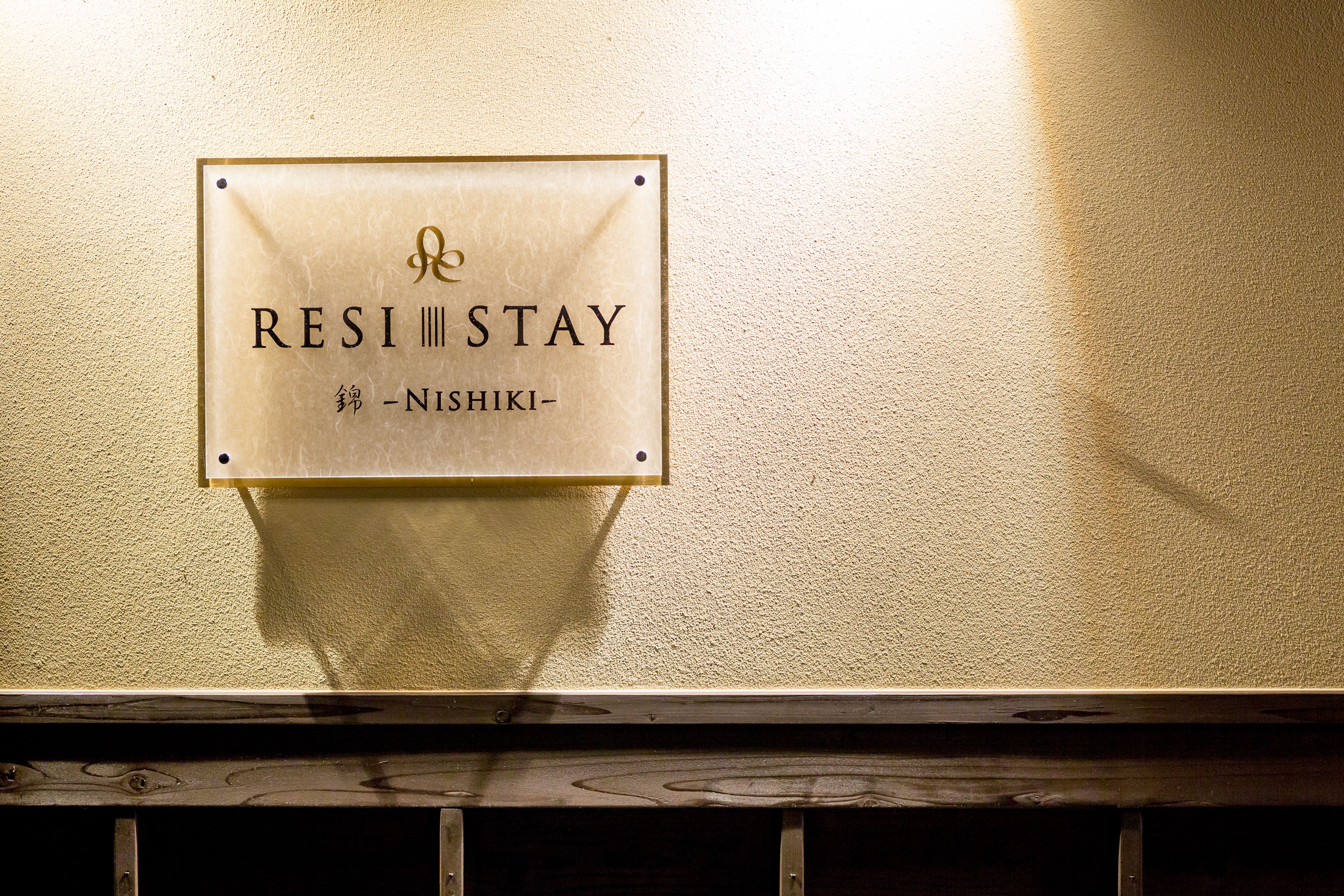 A sign with the text "RESI STAY" and "NISHIKI" on a wall.