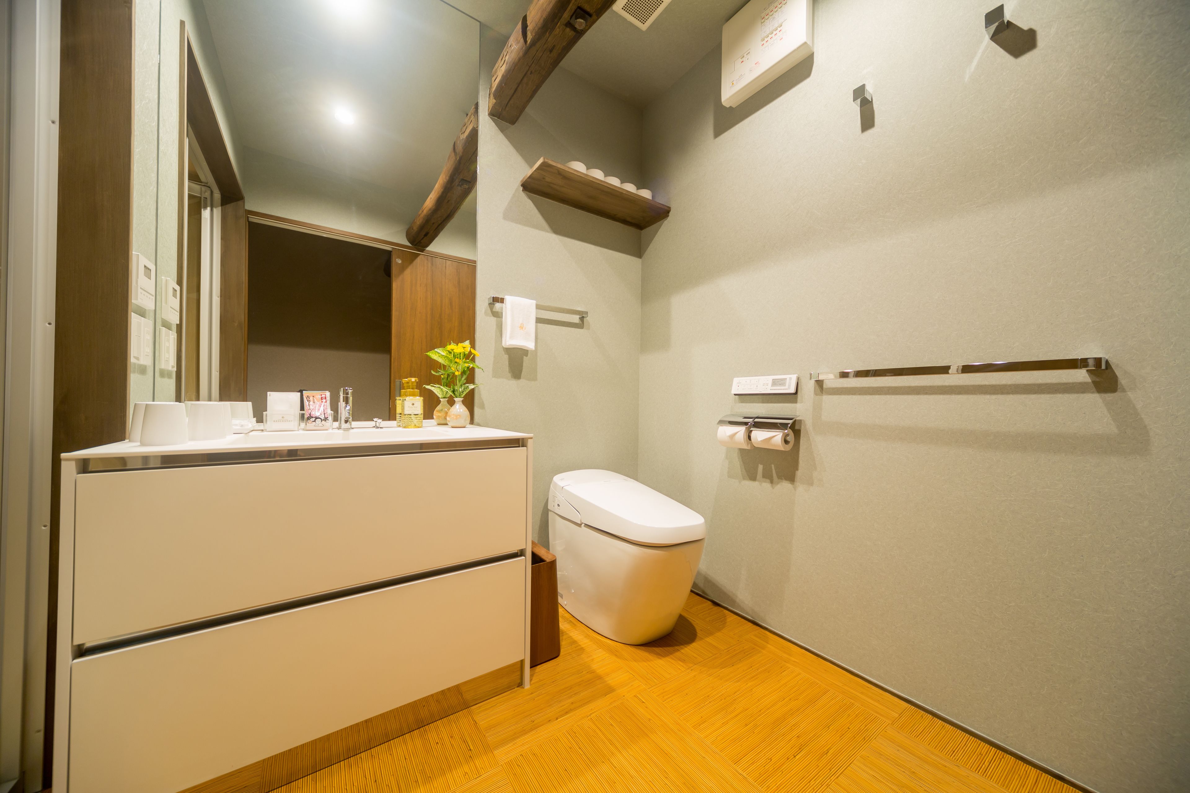 Un baño moderno con suelo de madera, inodoro blanco, lavabo con espejo y toallero.