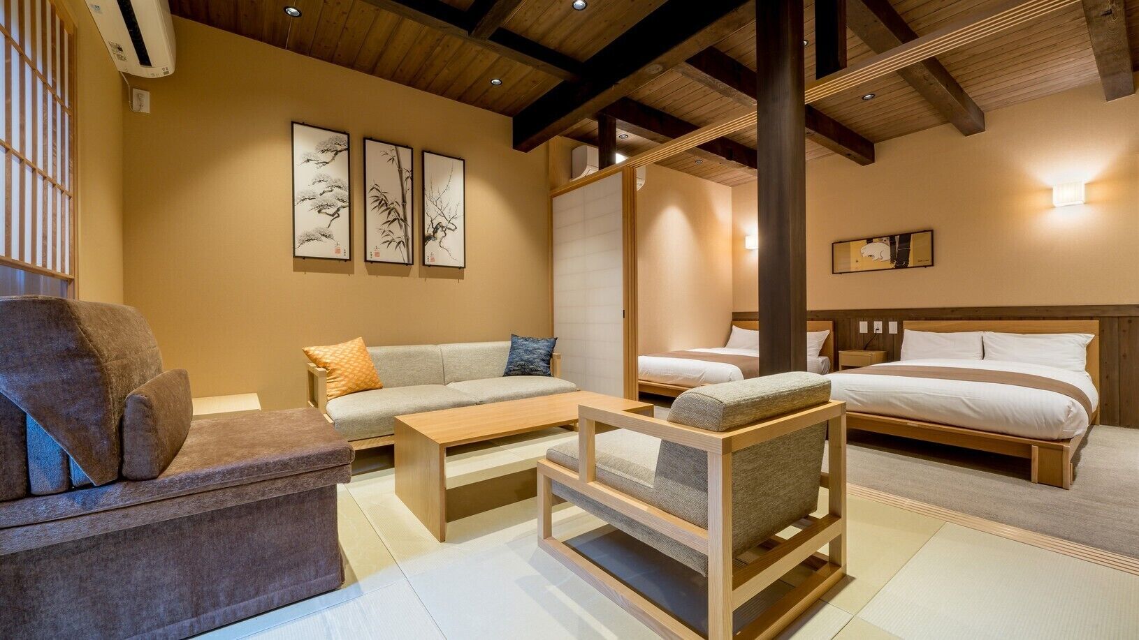 A hotel room with a sofa, a chair, a bed, a wooden coffee table, and artwork on the wall.