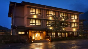 A multi-story hotel with a traditional architectural style, featuring a well-lit entrance and a parking area in front. - Hirayuonsen Yamatokan (Takayama)