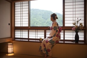 A room with tatami flooring, a shoji screen, a traditional Japanese-style lamp, and a vase with flowers.