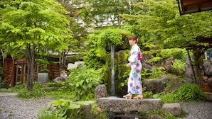 A traditional Japanese building with a wooden exterior, surrounded by lush greenery and a small waterfall. - Hirayuonsen Yamatokan (Takayama)