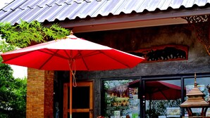 A building with a tiled roof, a wooden bench, a large red umbrella, and a brick wall. - Sawasdee Sukhothai Resort (Sukhothai)