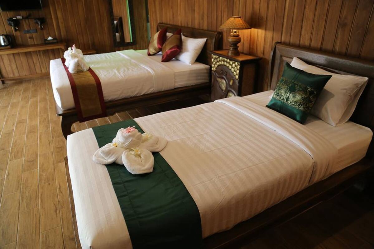 Dos camas dobles con sábanas blancas, cubrecamas verdes y almohadones decorativos. Se observa un cabecero de madera, una mesita de noche con una lámpara y un televisor montado en la pared.