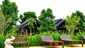 A pool area with lounge chairs and a statue, surrounded by lush greenery and traditional-style buildings. - Sawasdee Sukhothai Resort (Sukhothai)