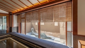 A modern interior with a stone bench, a wooden ceiling, and a view through a bamboo screen.