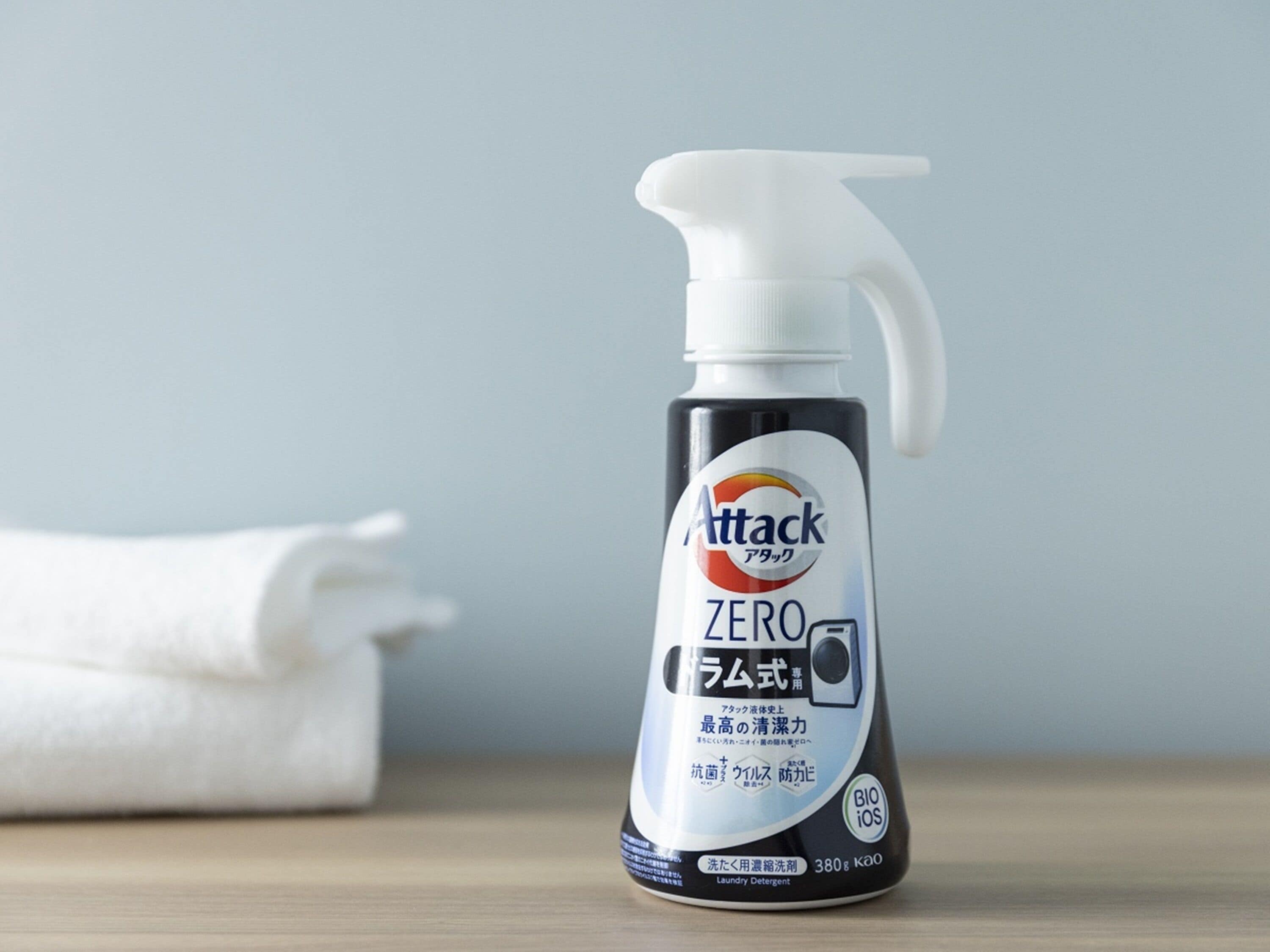 A bottle of Attack Zero laundry detergent on a wooden surface with a white towel in the background.