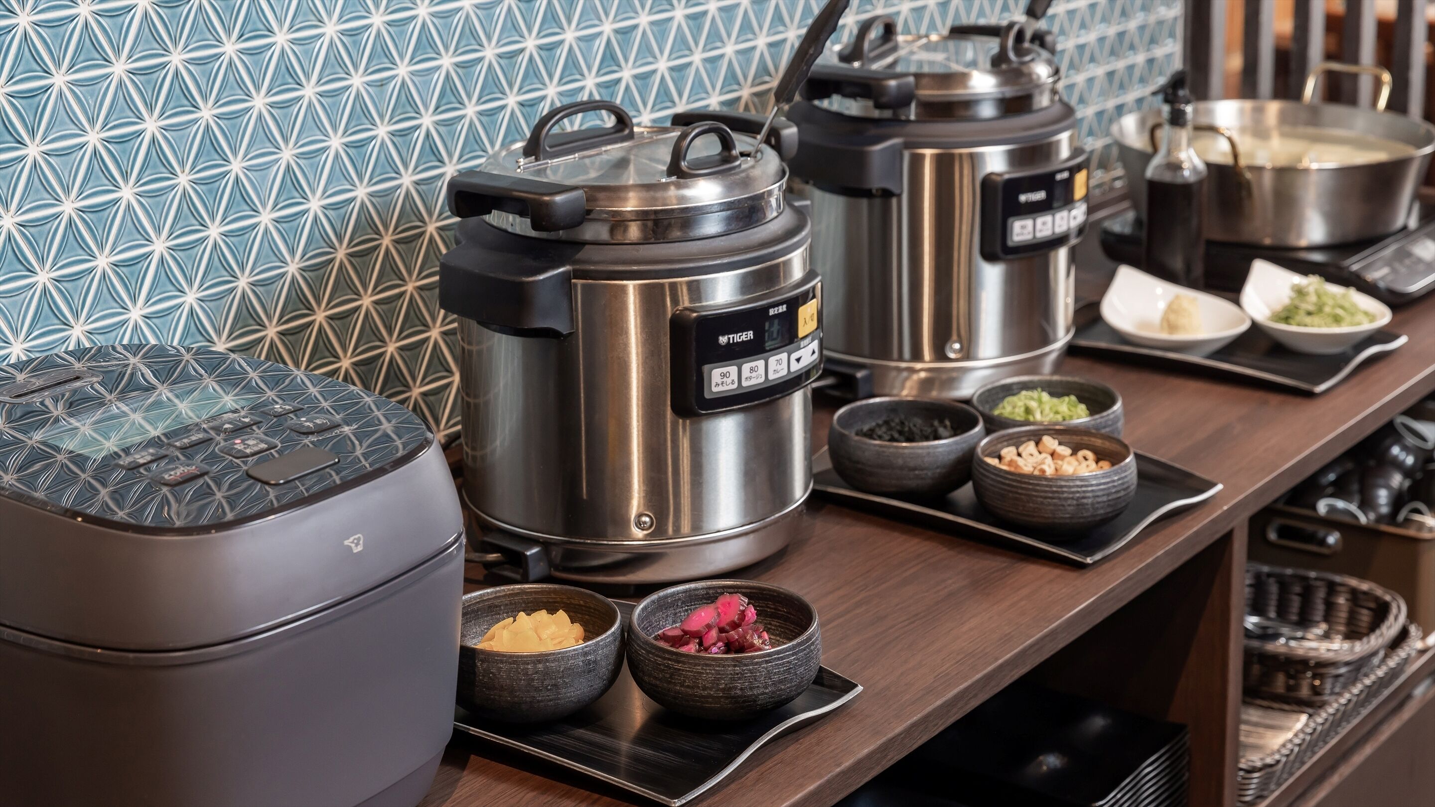 A kitchen with various cooking appliances, including a rice cooker, a pressure cooker, and a pot on the stove. There are also bowls with different food items on the counter.