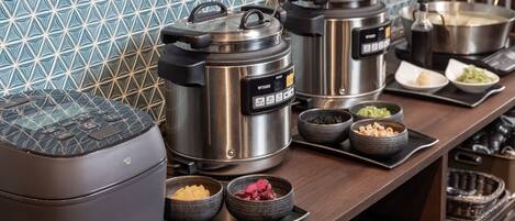 A kitchen with various cooking appliances, including a rice cooker, a pressure cooker, and a pot on the stove. There are also bowls with different food items on the counter.
