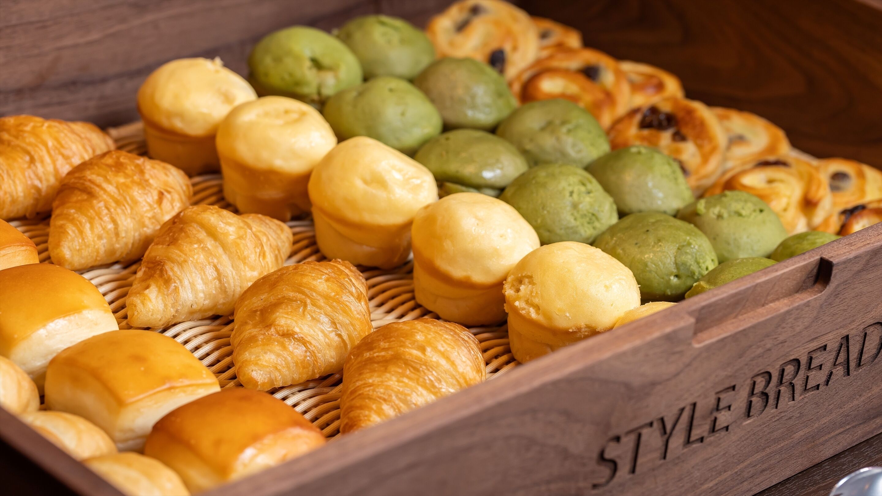 A wooden box labeled "STYLE BREAD" containing various baked goods like croissants and muffins.