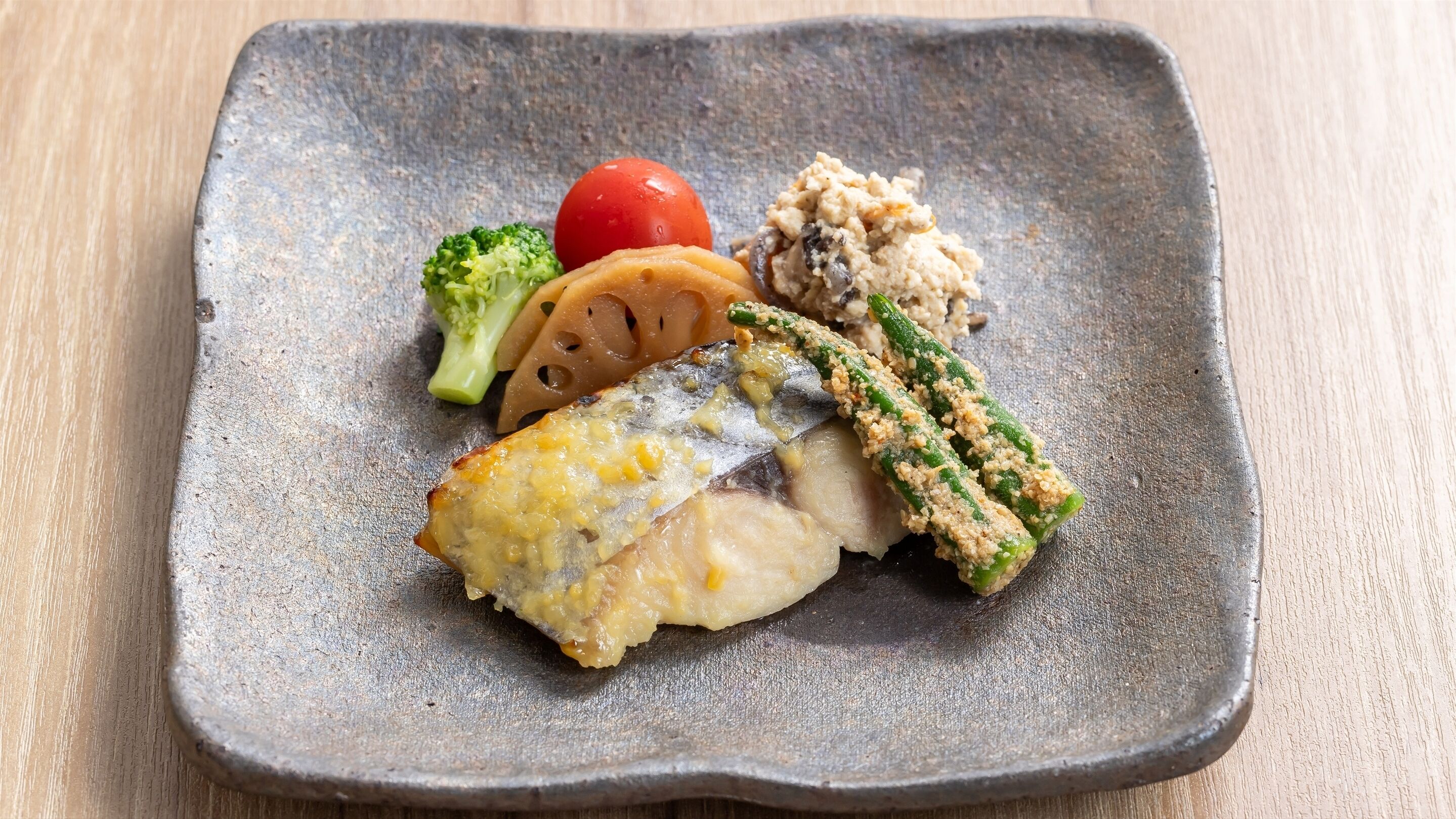Een vierkant bord met een stuk vis, een plak tomaat, een stuk broccoli en een portie rijst.