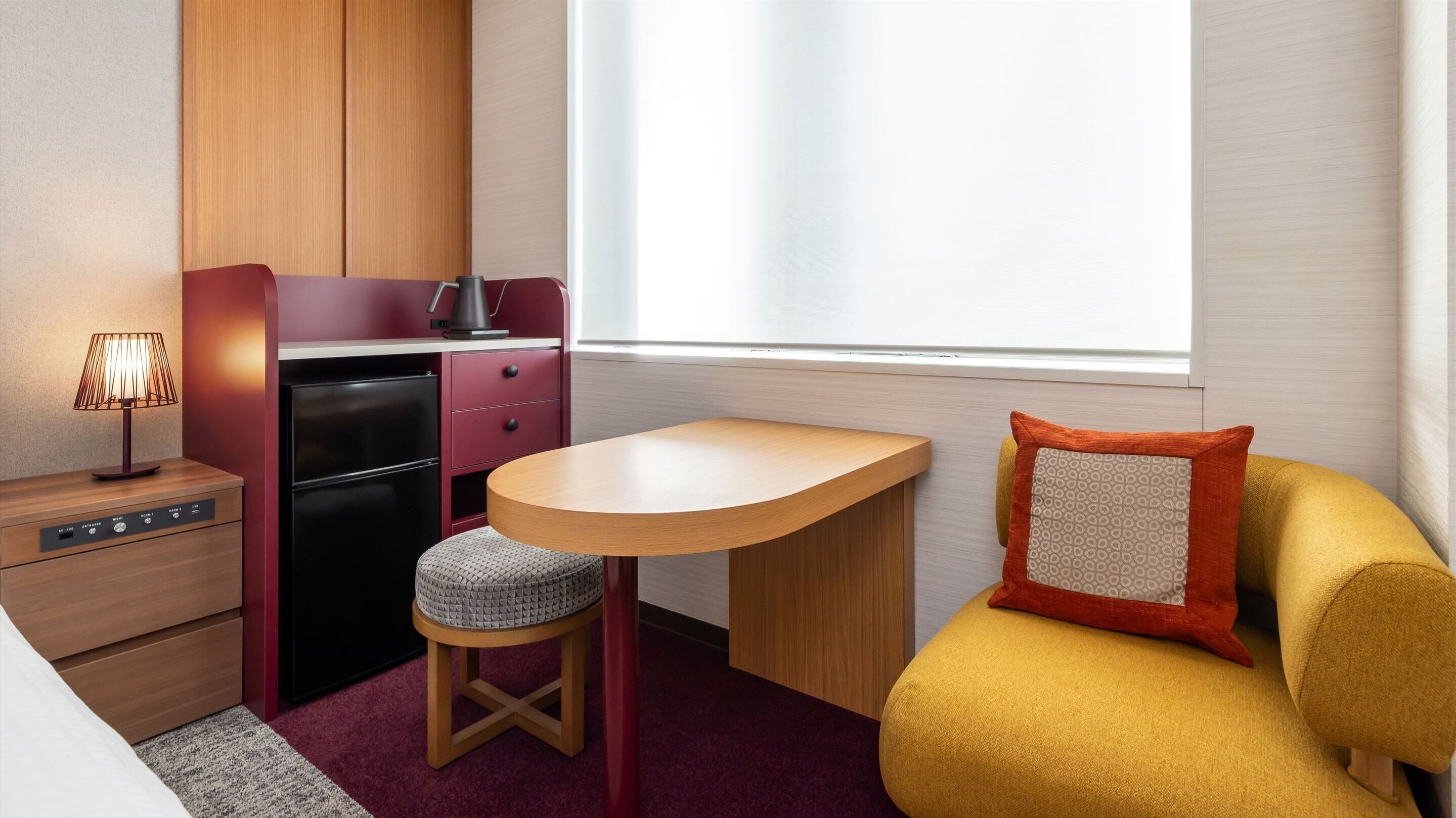 A compact room with a kitchenette, a small dining table, a sofa, and a lamp.