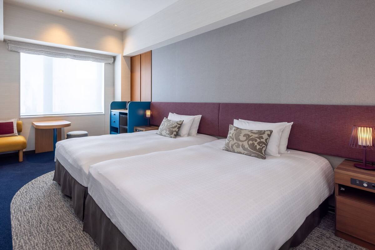 Une chambre d’hôtel avec deux lits, un bureau, une chaise et une fenêtre.