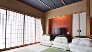 Una habitación japonesa tradicional con suelo de tatami, futón, puertas correderas y televisor.