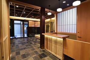 A reception area with a wooden counter, a tiled floor, and a view of the outside through large sliding doors. - Ryokan hanare Tengachaya (Osaka)