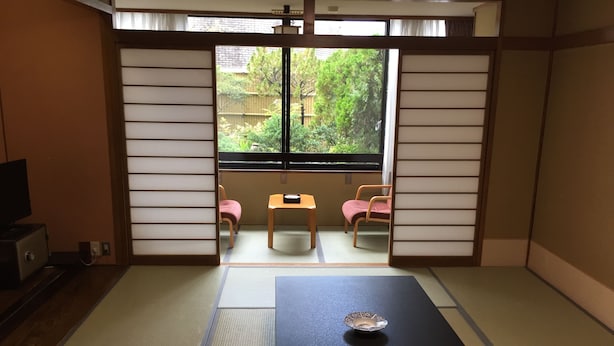 Une pièce de style japonais traditionnel, avec un sol recouvert de tatamis, une petite table ornée d’un bol décoratif et deux chaises.