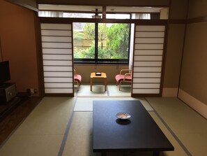 A traditional Japanese room with tatami flooring, a low table with a decorative bowl, and two chairs. - Serabekkan (Hiroshima)